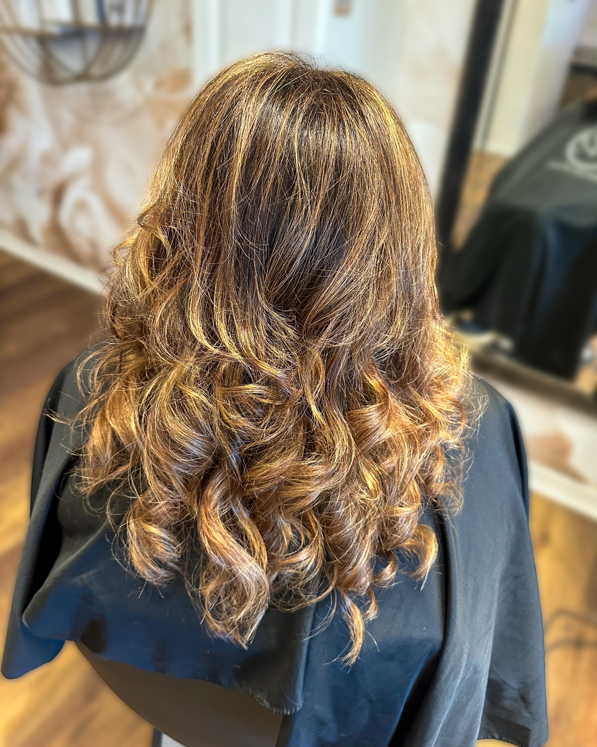 Dimensional brunette hair finished in soft curls at Maison de Cheveux.