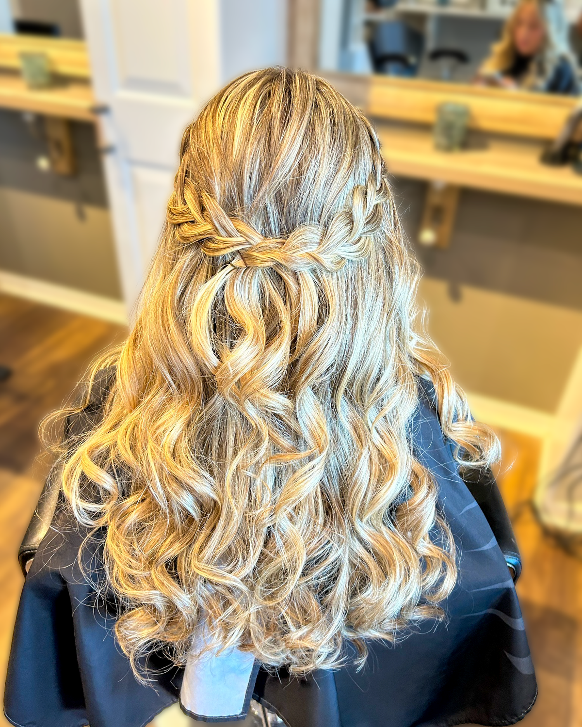 Blonde hair with a crown braid and polished curls at Maison de Cheveux.
